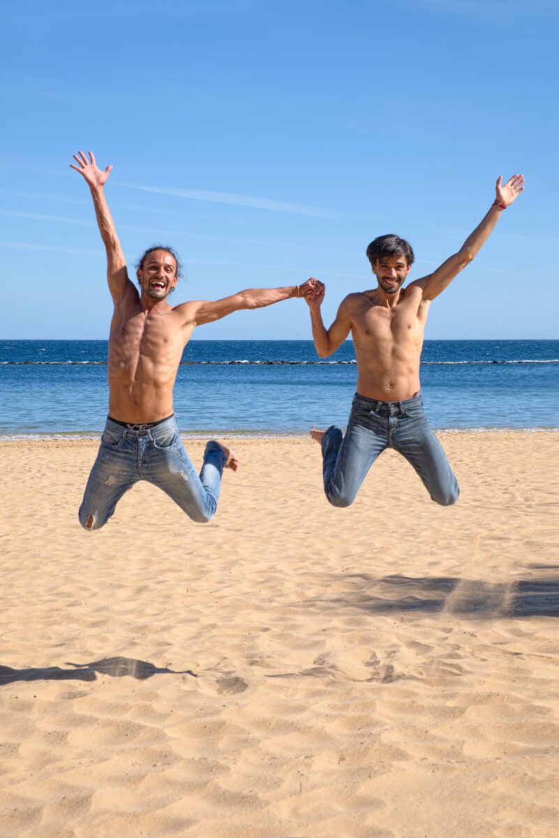 Two happy gay men jumping on the beach, celebrating their love and enjoying life after 40"