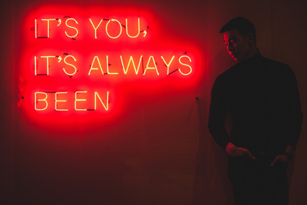 Asian man standing next to neon sign that reads "It's you - it's always been