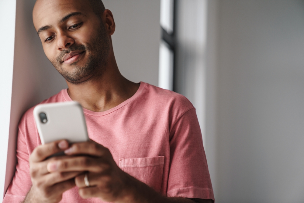 Gay guy using Grindr while in a relationship leaning on a wall with phone in his hand